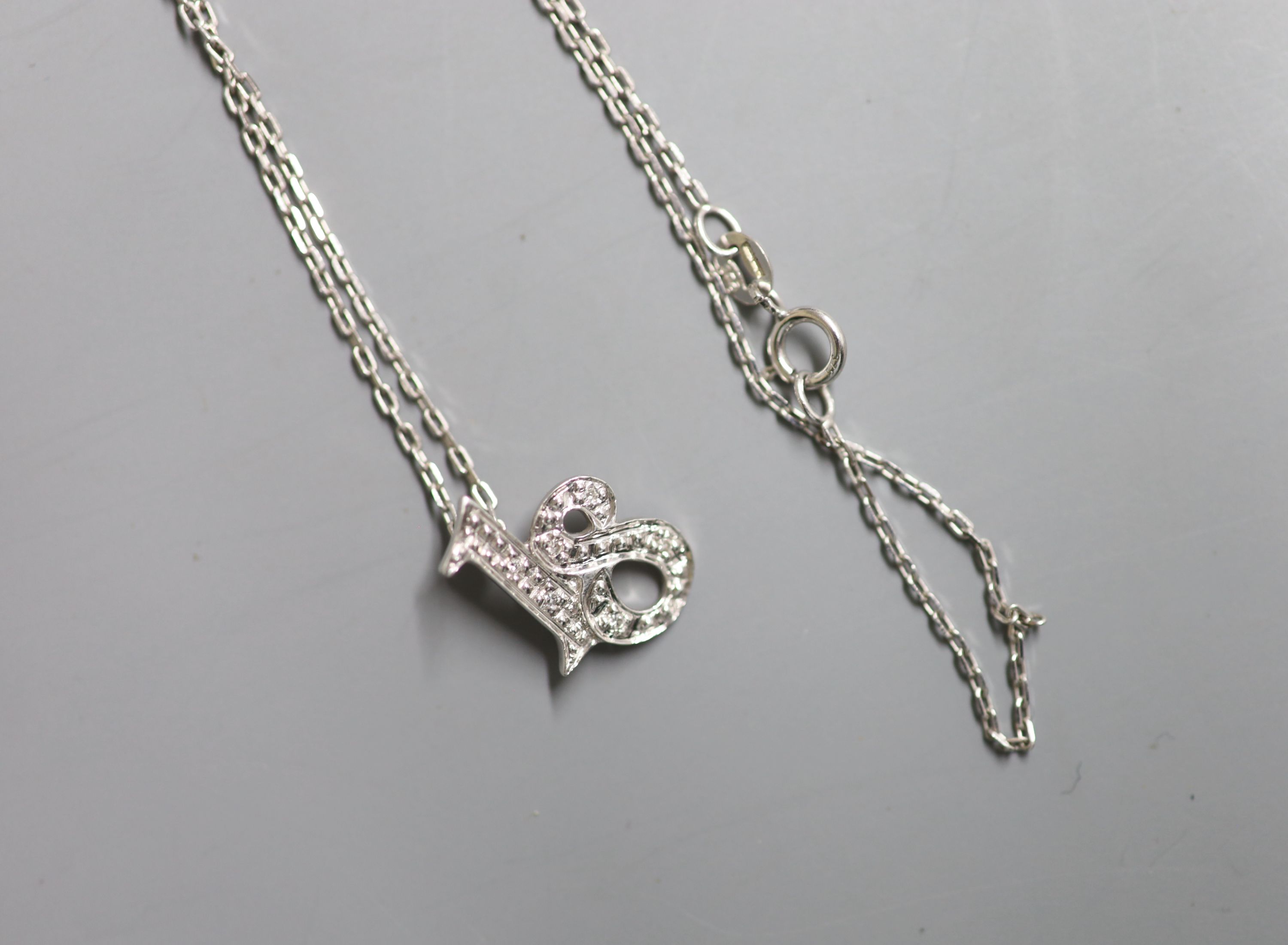 A modern 9ct white gold and diamond chip set 18 pendant, 14mm, on a 9ct white gold fine link chain, 43cm, gross 2.5 grams.